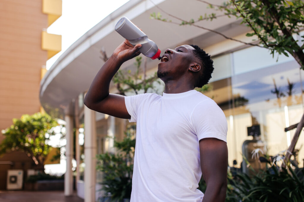 Portrait of Young African American man drinking water from a bottle. Male handsome sports person doing workout outdoor in the summer